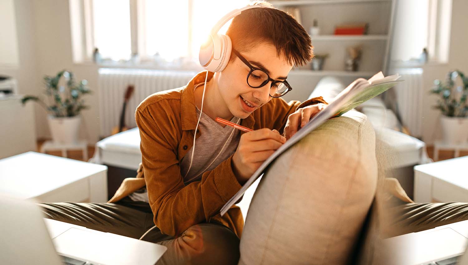 Teenager wearing headphones and writing in a notebook on a couch at home