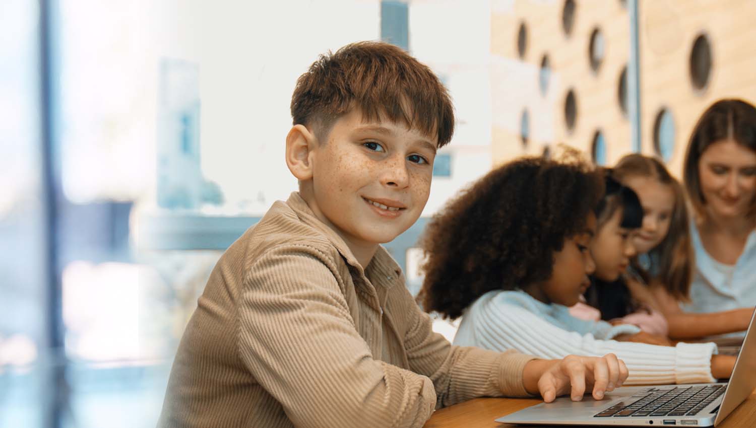 Smiling boy using a laptop with other students working together in the background