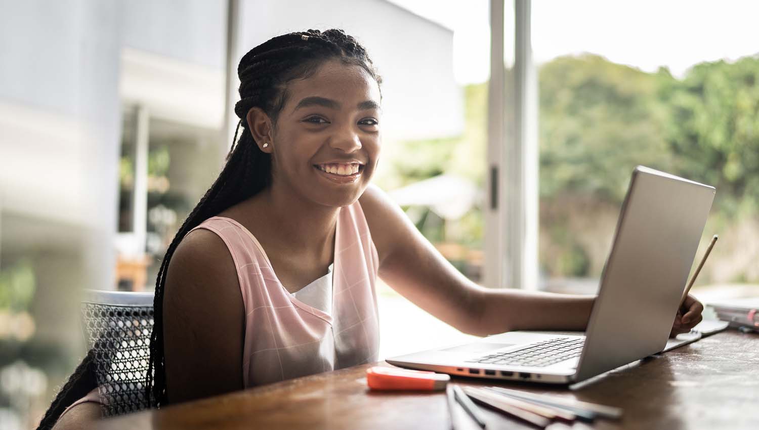 Smiling student working on a laptop at a desk near a window with natural light